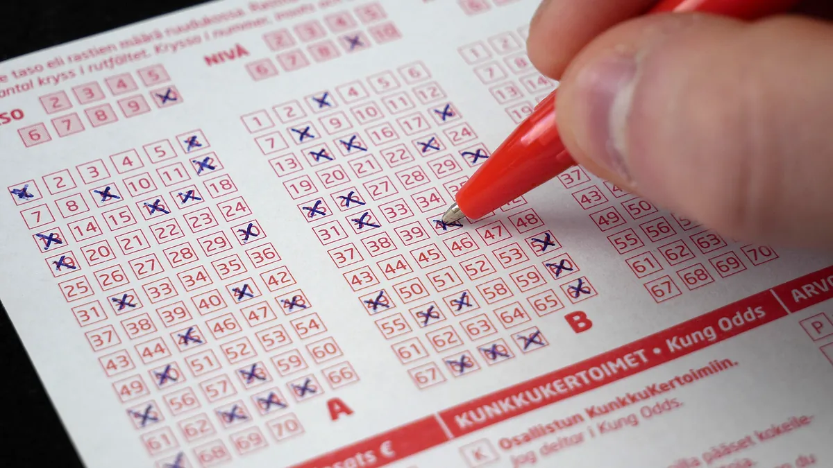Hand marking numbers on a keno ticket with a red pen